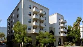 Exterior view of Tides Senior Apartments, a multi-story residential building with balconies, landscaped trees, and a covered ground-level entrance.