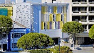 Exterior view of Step Up on Fifth, a modern urban building with white paneling and colorful screened balconies along a city street.