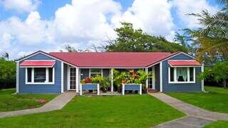 Kahuku Elderly Hauʻoli Hale features a single story affordable housing community by EAH Housing with plantation style design, red roof, and landscaped yard in a lush Hawaii setting