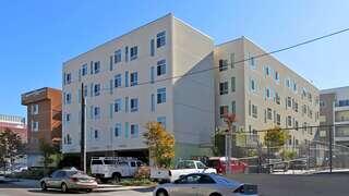 Exterior view of Seven Maples Senior Apartments, a modern multi-story building with clean lines, light-colored walls, and parking beneath the structure.