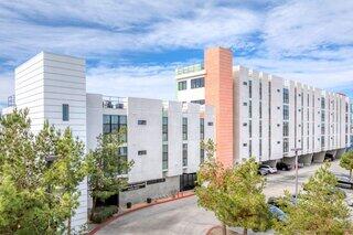 Exterior view of Sagebrush Apartments, a contemporary multi-story community with white and gray facades, an orange accent tower, and a parking area.