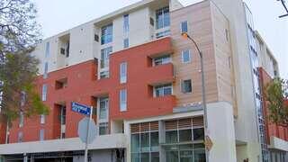 Exterior view of Rosewood Gardens Senior Apartments, a modern multi-story building with red and white paneling and ground-floor windows along a city street.