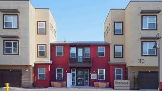 Exterior view of Riverwalk Apartments, a contemporary community with red and beige buildings, a central entrance, and leasing office signage.