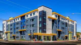 Exterior view of Pimentel Place, a contemporary multi-story building with blue, gray, and yellow accents at a street corner.