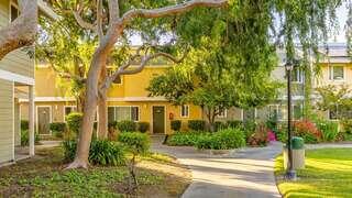 Los Robles features a two story affordable housing community by EAH Housing with warm toned exterior, shaded walkways, mature trees, and landscaped courtyard in a residential neighborhood