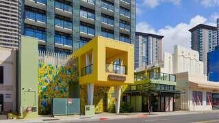 A vibrant yellow structure with unique architectural features stands beside modern buildings, showcasing colorful murals and urban development.