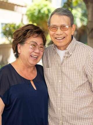 A happy couple smiles warmly together outdoors, exuding joy and affection in a bright, cheerful setting.