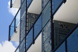 Modern architectural design featuring layered balconies with decorative metal panels and glass railings against a clear blue sky.