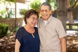 A joyful couple shares a laugh outdoors, surrounded by greenery, showcasing warmth and affection in a sunny setting.