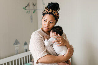 A woman gently holds a sleeping baby in a cozy room, exuding tenderness and maternal love, with soft decor in the background.