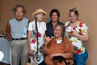 Residents gather at a community event, smiling together in a welcoming indoor setting, with one resident seated in a wheelchair and others standing nearby, reflecting connection and a sense of belonging at an EAH Housing property, Aloha Ia Halewiliko.